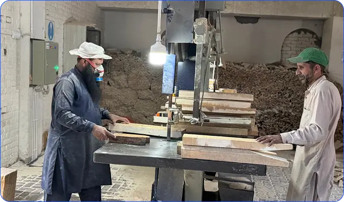 Two workers operating an industrial band saw in a workshop