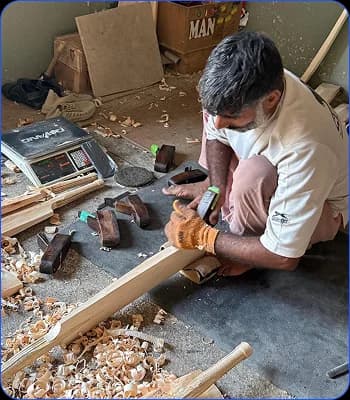 Craftsperson hand-planing a wooden cricket bat on the workshop floor